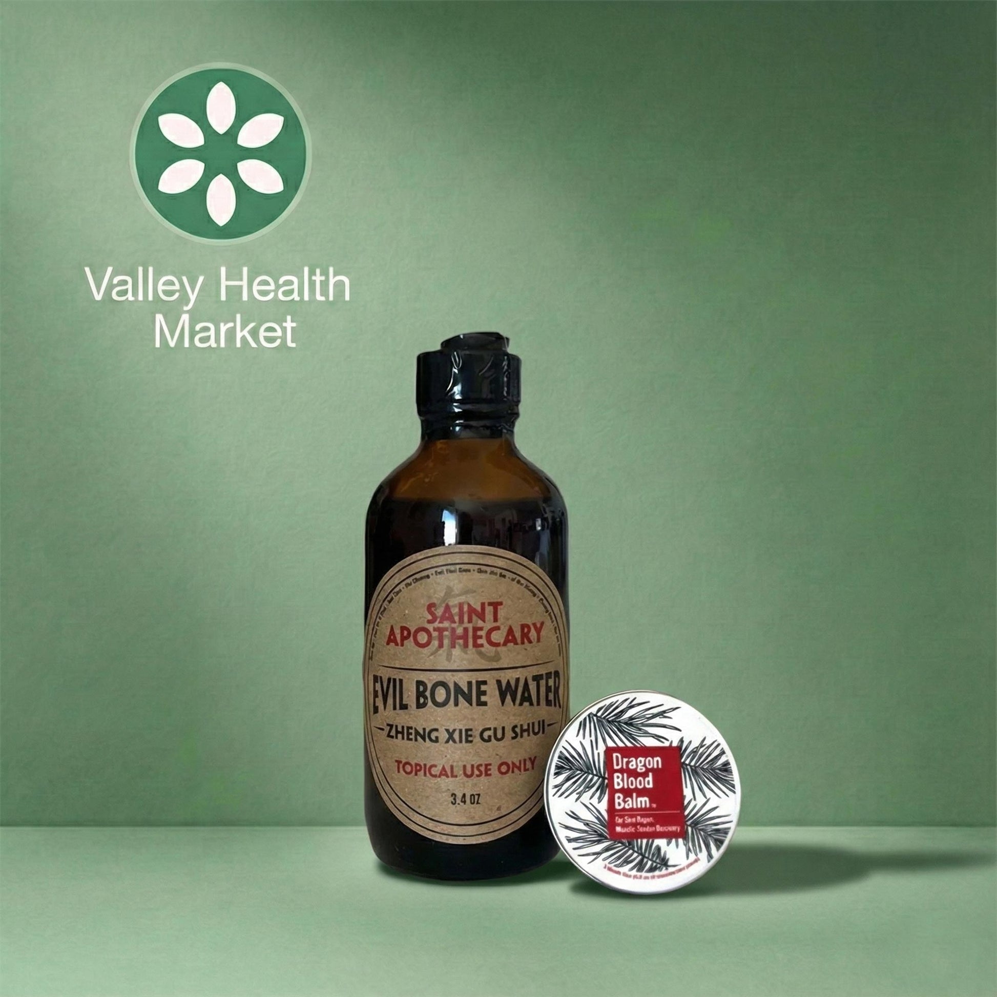 Bottle of Saint Apothecary Evil Bone Water and Dragon Blood Balm on a green background with Valley Health Market logo.